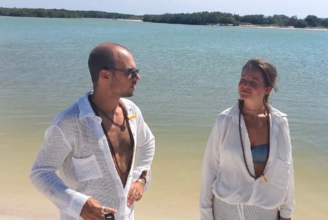 Man and woman in casual beachwear standing by a sunny lakeside.
